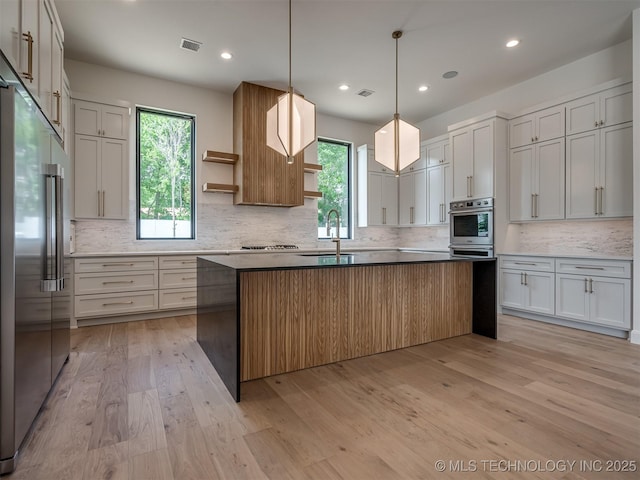 kitchen with a center island with sink, sink, light hardwood / wood-style floors, white cabinetry, and stainless steel appliances