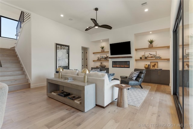 living room with light wood-type flooring, built in features, and ceiling fan