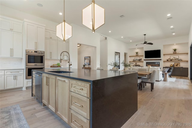 kitchen featuring ceiling fan, sink, double oven, backsplash, and an island with sink