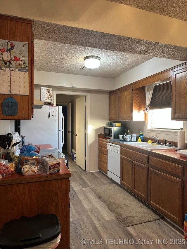 kitchen with a textured ceiling, light wood-type flooring, white appliances, and sink