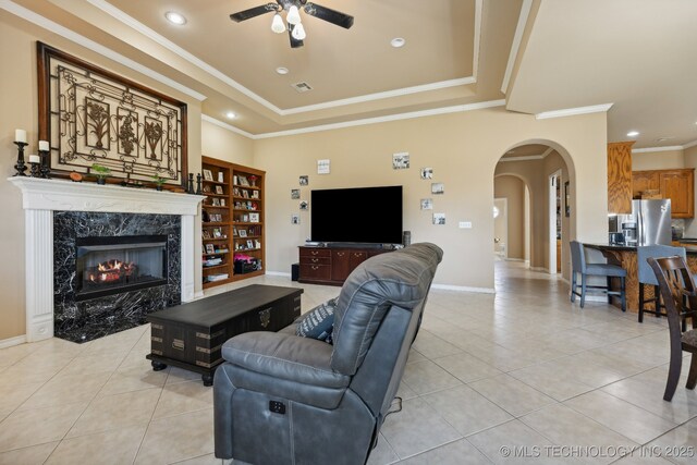 tiled living room with ceiling fan, ornamental molding, a high end fireplace, and a tray ceiling