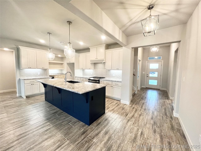 kitchen featuring a kitchen island with sink, sink, a chandelier, white cabinetry, and stainless steel range with gas stovetop