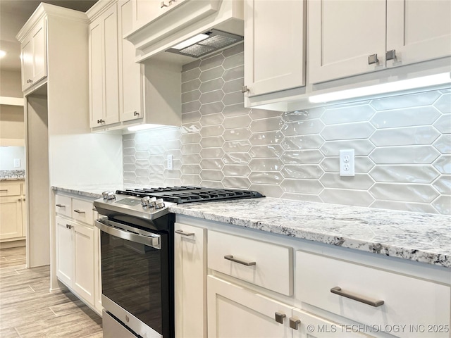 kitchen with backsplash, stainless steel range with gas cooktop, white cabinets, and light stone counters