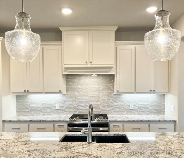 kitchen with decorative backsplash, gas range, white cabinetry, and hanging light fixtures