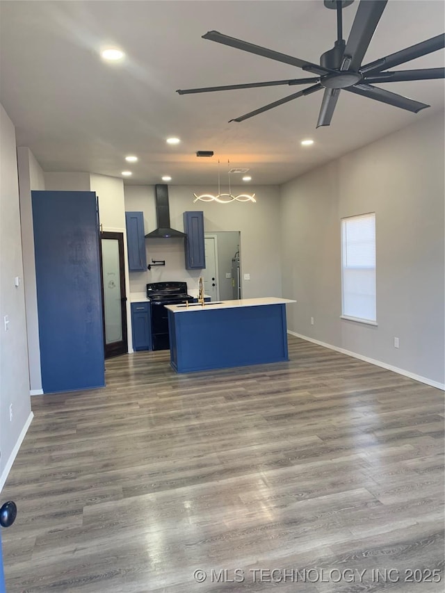 kitchen with a kitchen island with sink, wall chimney exhaust hood, blue cabinetry, black / electric stove, and wood-type flooring