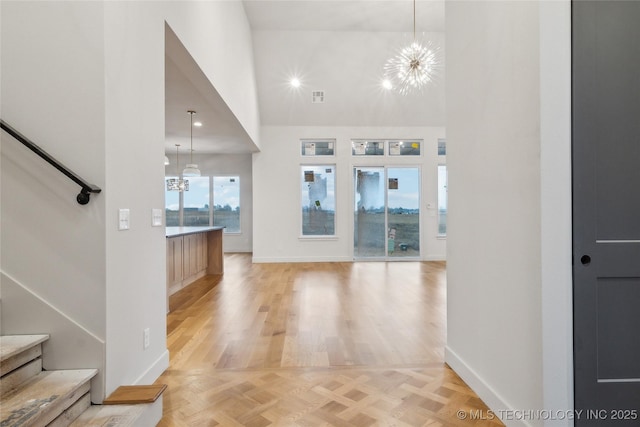 foyer entrance featuring light parquet flooring, a towering ceiling, and a notable chandelier