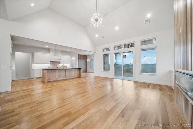 unfurnished living room featuring high vaulted ceiling, sink, light hardwood / wood-style floors, and a notable chandelier