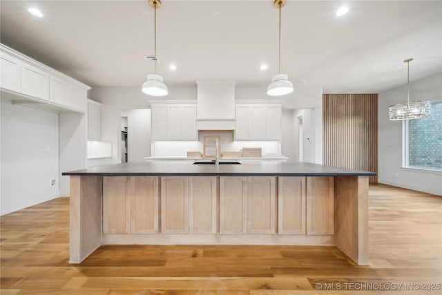 kitchen featuring white cabinetry, wall chimney range hood, pendant lighting, and a large island with sink