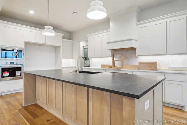 kitchen with hanging light fixtures, a center island with sink, white cabinets, and appliances with stainless steel finishes