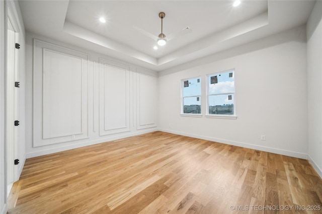 empty room featuring ceiling fan, a raised ceiling, and light hardwood / wood-style floors