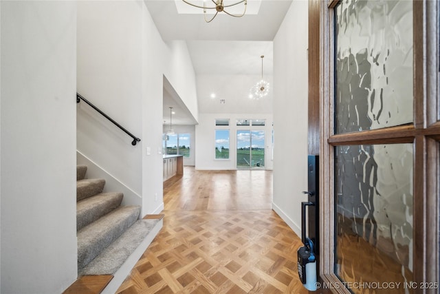 foyer entrance featuring baseboards, a high ceiling, a notable chandelier, and stairway