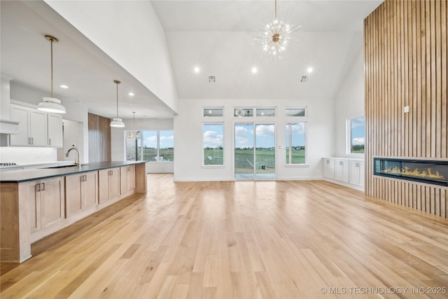 unfurnished living room featuring recessed lighting, a sink, a glass covered fireplace, light wood-style flooring, and high vaulted ceiling
