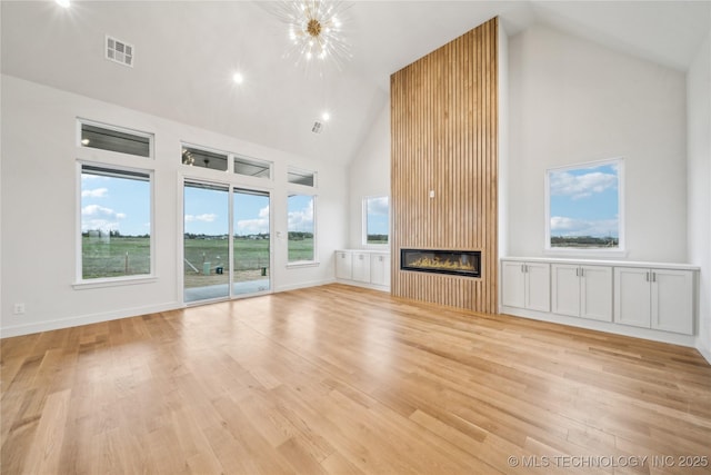 unfurnished living room featuring high vaulted ceiling, a glass covered fireplace, a wealth of natural light, light wood-style flooring, and visible vents