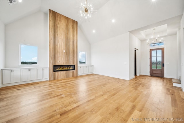 unfurnished living room featuring high vaulted ceiling, a notable chandelier, light wood-style flooring, and a fireplace