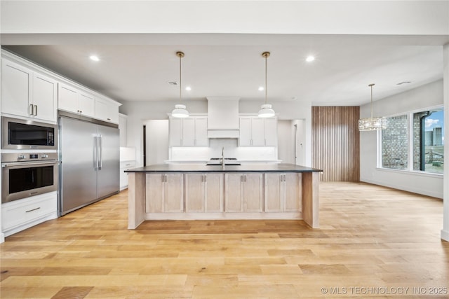 kitchen featuring built in appliances, premium range hood, dark countertops, and light wood-style floors