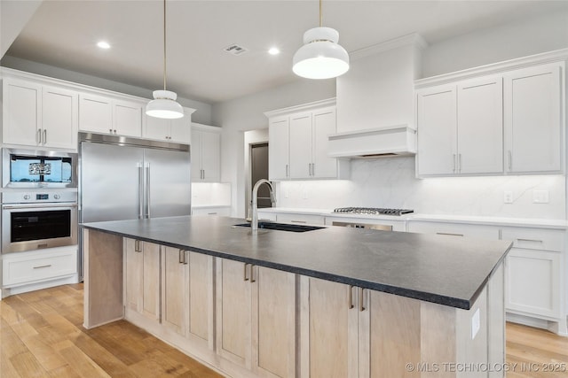 kitchen featuring dark countertops, custom exhaust hood, tasteful backsplash, a sink, and built in appliances