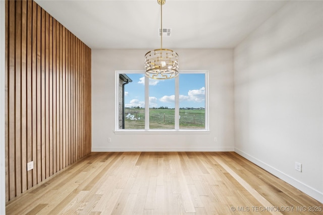 unfurnished dining area with baseboards, light wood finished floors, a chandelier, and visible vents
