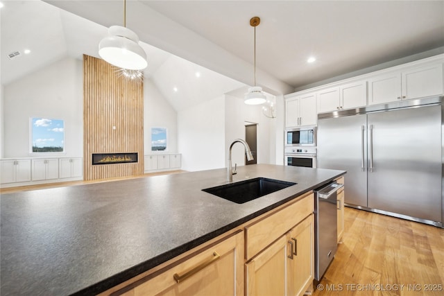 kitchen with dark countertops, a sink, decorative light fixtures, a fireplace, and built in appliances