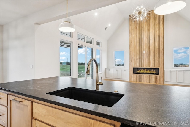 kitchen featuring high vaulted ceiling, dark countertops, a sink, a large fireplace, and decorative light fixtures