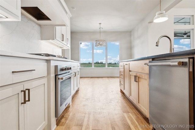 kitchen with light brown cabinets, light wood-style flooring, decorative light fixtures, and appliances with stainless steel finishes