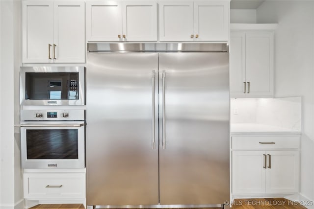 kitchen with white cabinets, light countertops, tasteful backsplash, and built in appliances