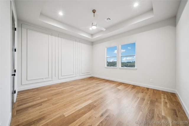 spare room featuring a tray ceiling, visible vents, baseboards, light wood-style floors, and a ceiling fan