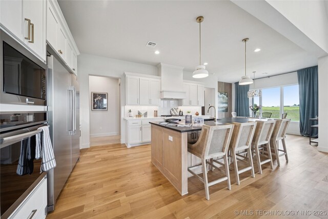 2509 E 134th Cir, Bixby, OK 74008 - kitchen with stainless steel appliances, a kitchen bar, an island with sink, white cabinets, and light wood-style floors