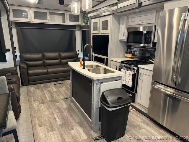 kitchen with white cabinetry, sink, stainless steel appliances, light hardwood / wood-style flooring, and a kitchen island with sink