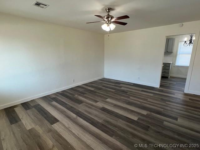 unfurnished room with ceiling fan with notable chandelier and dark wood-type flooring