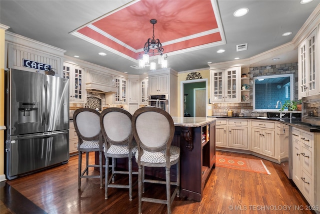 kitchen with a center island, stainless steel appliances, crown molding, decorative light fixtures, and a tray ceiling