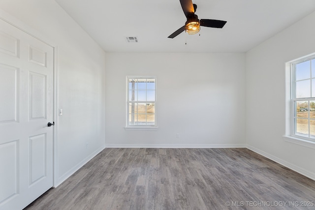 spare room featuring baseboards, visible vents, wood finished floors, and a wealth of natural light