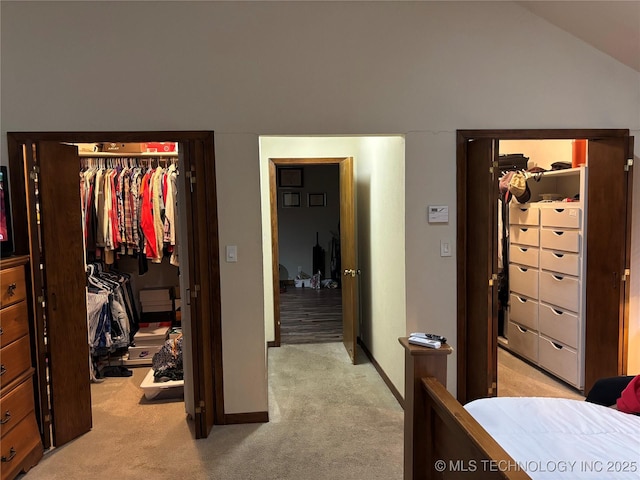 bedroom with lofted ceiling, a closet, light colored carpet, a spacious closet, and baseboards