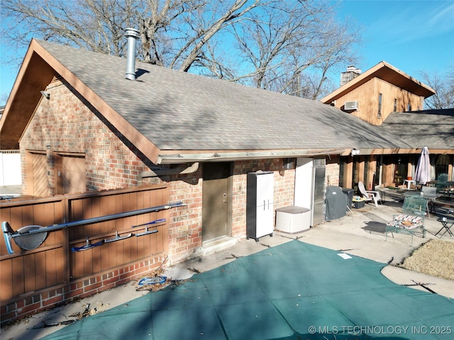 rear view of house with a shingled roof, a patio, and brick siding