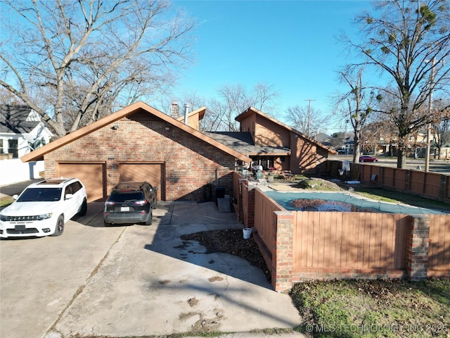 view of home's exterior with an attached garage, brick siding, fence, driveway, and a chimney