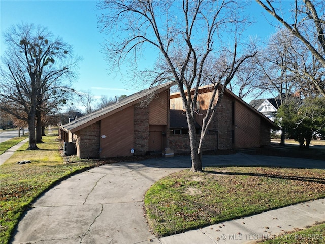 view of front facade with a front yard, concrete driveway, brick siding, and cooling unit