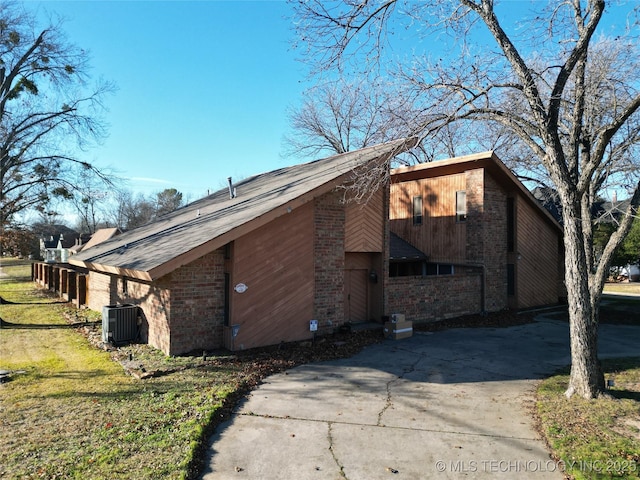 view of side of property with concrete driveway, a yard, central AC, and brick siding