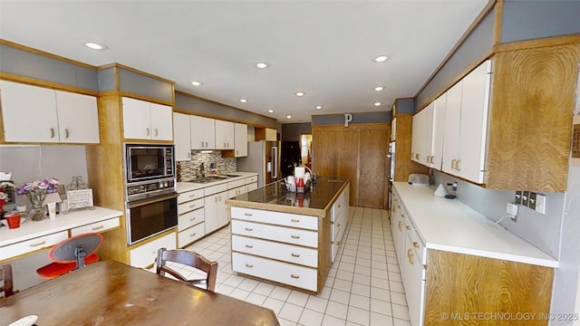 kitchen with a center island, tasteful backsplash, white cabinets, light tile patterned flooring, and black appliances