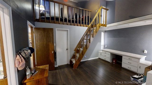 interior space with a towering ceiling, built in desk, baseboards, and wood finished floors