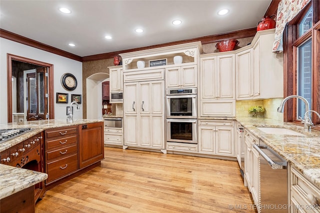 kitchen with sink, tasteful backsplash, light stone counters, built in appliances, and light wood-type flooring