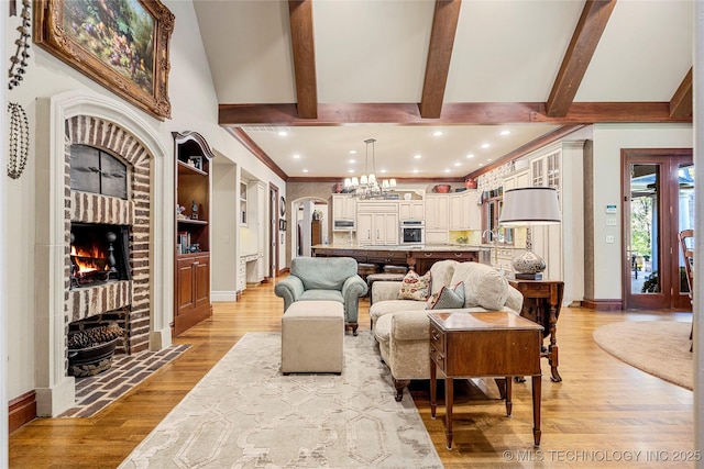 living room featuring beam ceiling, light wood-type flooring, built in features, and a brick fireplace