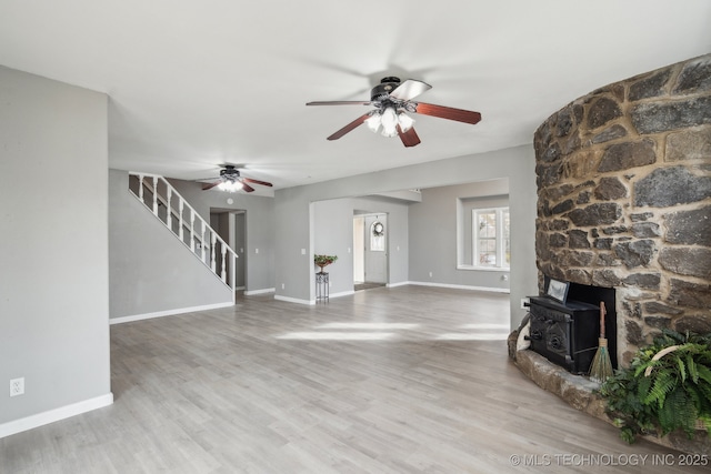 unfurnished living room with a wood stove, hardwood / wood-style floors, and ceiling fan