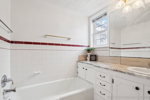 bathroom with vanity, a bathing tub, a textured ceiling, and tile walls