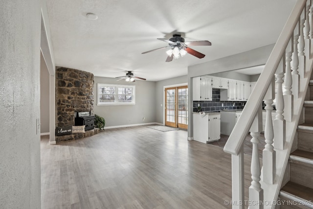 unfurnished living room with a textured ceiling, a wood stove, ceiling fan, and light wood-type flooring