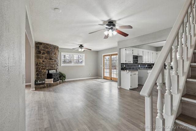 201 Sandy Cir, Tahlequah, OK 74464 - unfurnished living room with a wood stove, stairs, wood finished floors, ceiling fan, and baseboards
