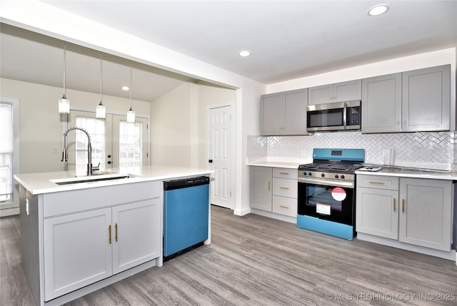 kitchen featuring gray cabinetry, sink, hanging light fixtures, stainless steel appliances, and an island with sink