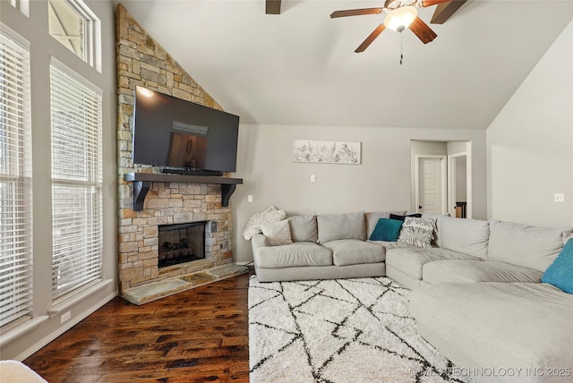 living room featuring dark hardwood / wood-style flooring, a stone fireplace, ceiling fan, and vaulted ceiling