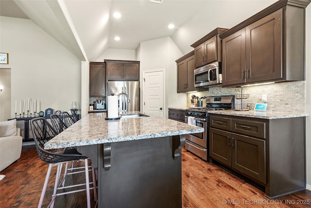 kitchen featuring a kitchen bar, appliances with stainless steel finishes, decorative backsplash, a kitchen island with sink, and lofted ceiling