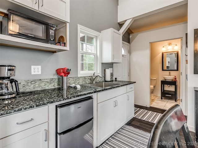 kitchen with white cabinets, backsplash, dark stone counters, and sink