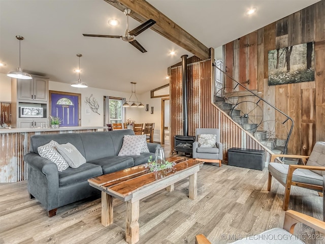 living room with wood walls, a wood stove, lofted ceiling with beams, ceiling fan, and light hardwood / wood-style floors