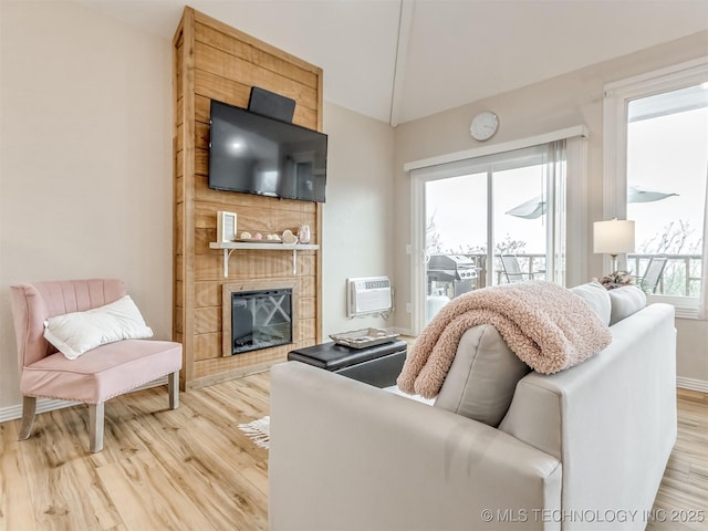 living room featuring a large fireplace, light hardwood / wood-style flooring, a wall mounted AC, and lofted ceiling